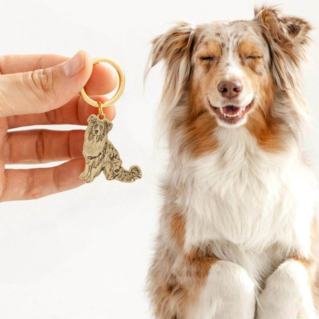 Hand holding a custom gold engraved pet ID tag keychain resembling an Australian Shepherd dog