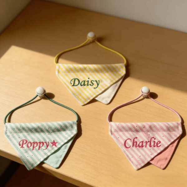 A top-down view of three personalized striped pet bandanas with adjustable drawstrings and custom embroidered names Daisy, Poppy, and Charlie